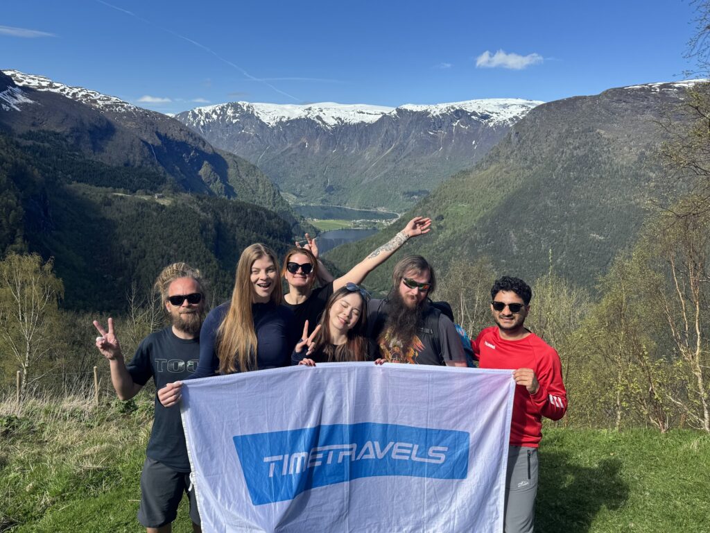 hikers smiling with Timetravels flag at the top of Fuglesteg hike, in front of the Norwegian fjords