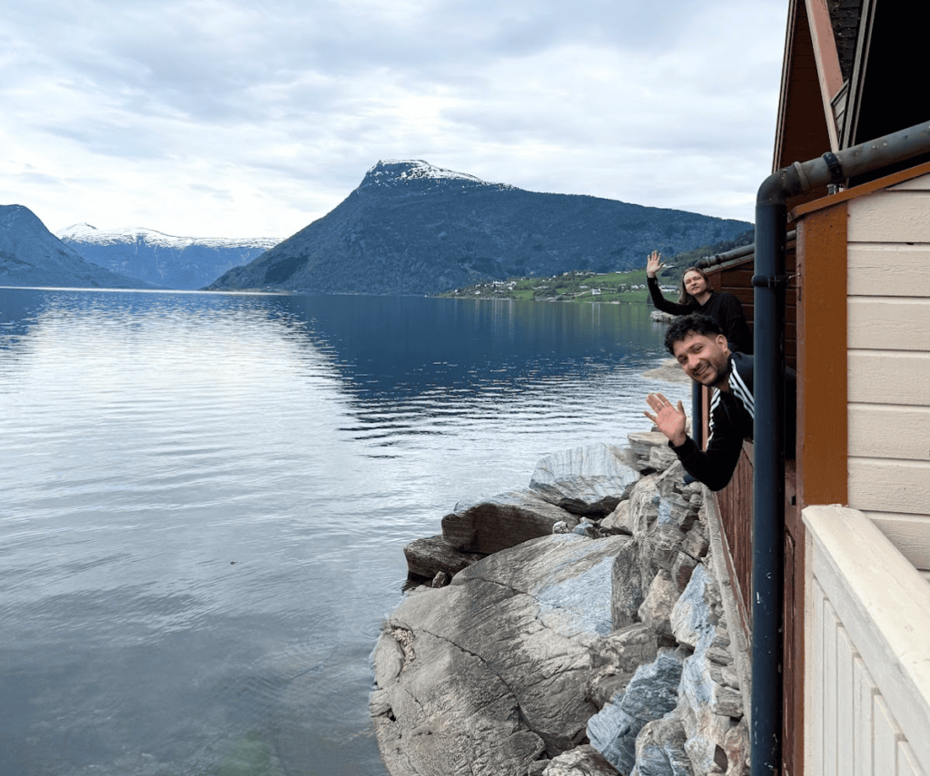two person waving from the terrace of the house with the view of fjords behind